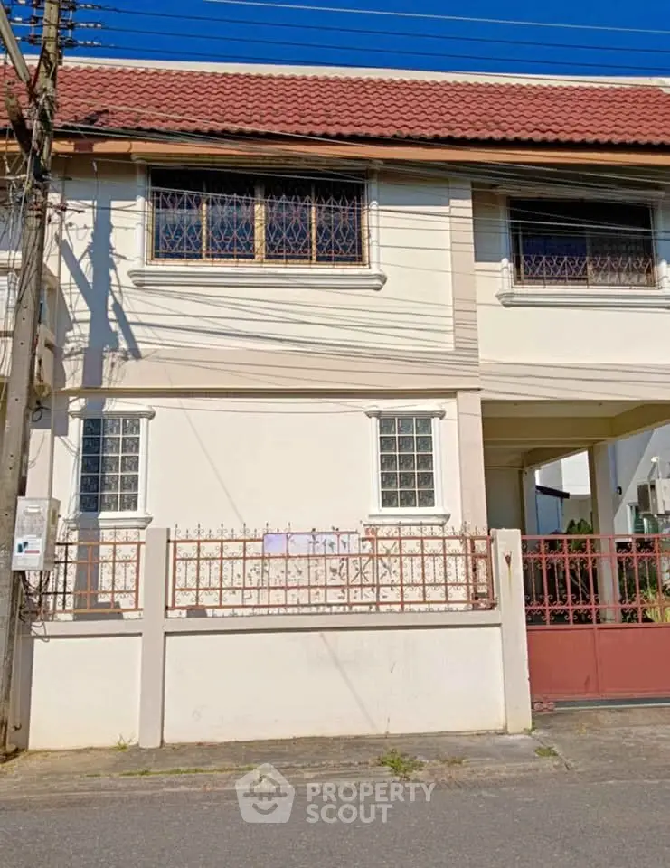 Charming two-story house with red roof and gated entrance in a quiet neighborhood.