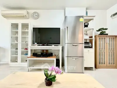 Modern living room with sleek appliances and stylish decor, featuring a TV, fridge, and air conditioning.