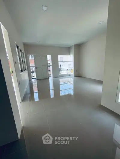 Spacious empty living room with glossy tiled floors and large windows offering natural light.