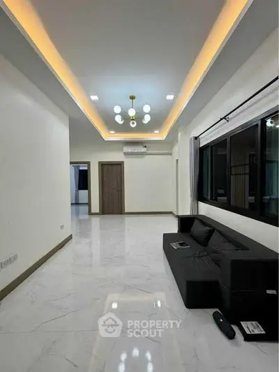 Spacious modern living room with sleek black sofa and elegant ceiling lighting.