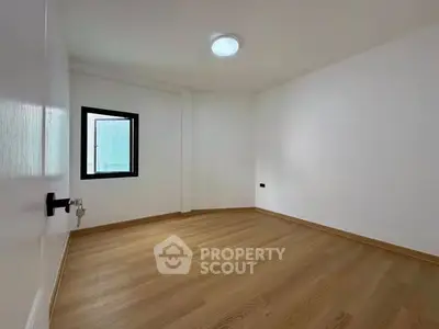 Spacious empty room with wooden flooring and a single window, ideal for customization.