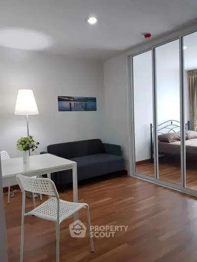 Modern living room with wooden flooring and glass sliding doors leading to a cozy bedroom.