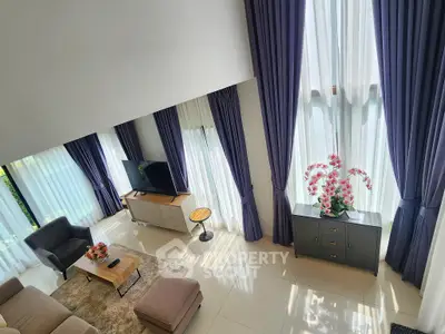 Spacious living room with high ceilings and elegant decor, featuring large windows and modern furniture.