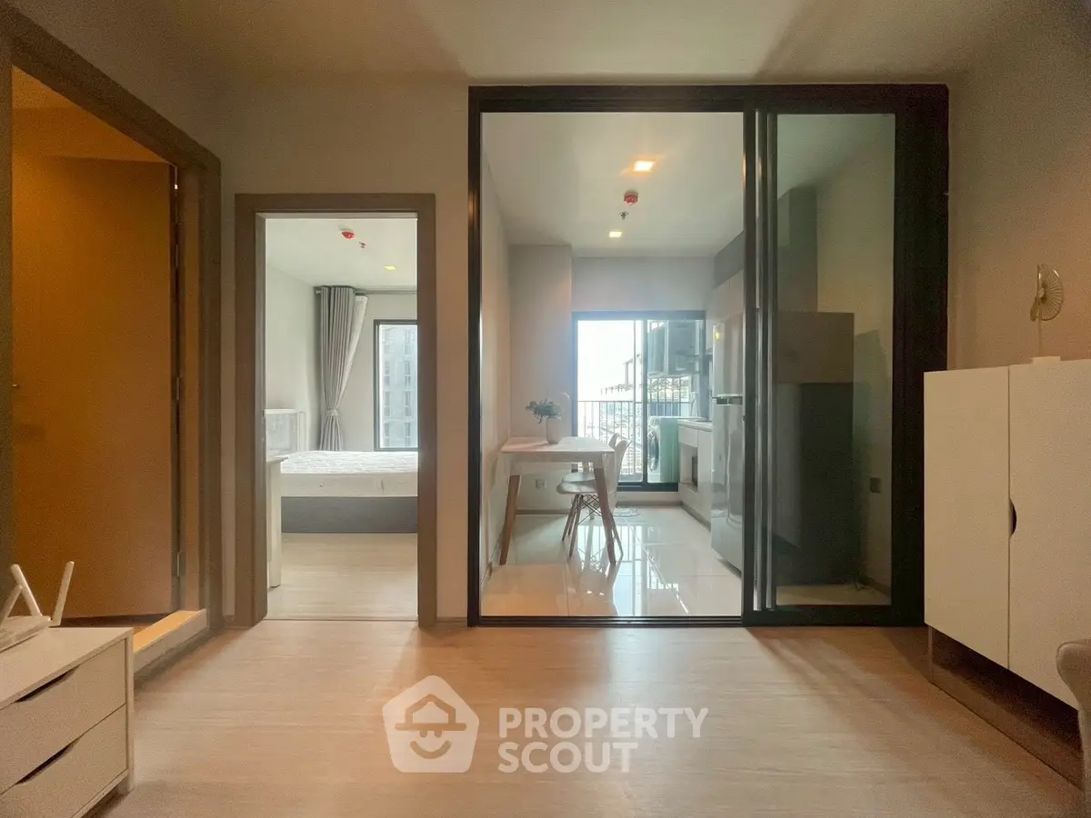 Modern apartment interior with open kitchen and bedroom view, featuring sleek design and natural light.