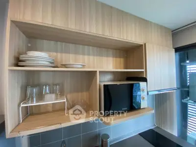 Modern kitchen with wooden cabinets and microwave, featuring open shelving and glassware.