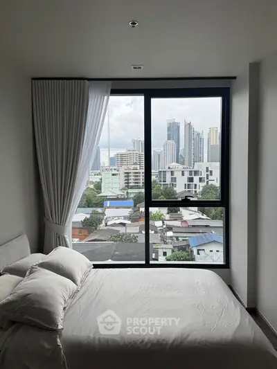 Modern bedroom with large window offering stunning city skyline view, featuring cozy bed and elegant curtains.