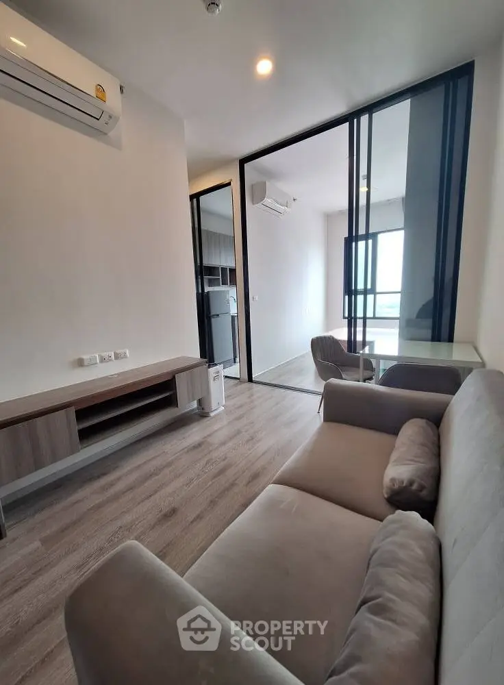 Modern living room with sleek furniture and glass partition, featuring air conditioning and natural light.