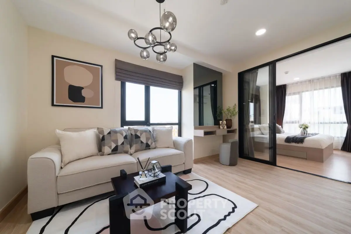 Modern living room with stylish decor and view into a cozy bedroom, featuring elegant lighting and wooden flooring.