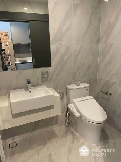 Modern bathroom with sleek fixtures and marble tiles, featuring a contemporary toilet and sink.