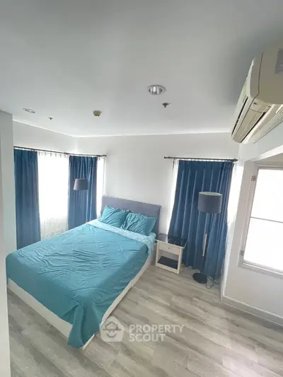 Modern bedroom with teal bedding and natural light, featuring sleek flooring and air conditioning.