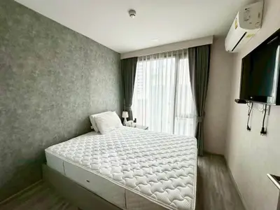 Modern bedroom with stylish decor, featuring a comfortable bed, wall-mounted TV, and large window with curtains.