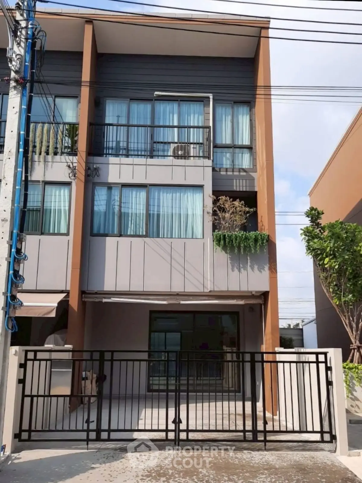 Modern three-story townhouse with gated entrance and large windows.