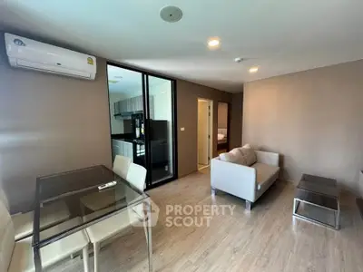 Modern living room with glass dining table and cozy sofa, open layout to kitchen area.