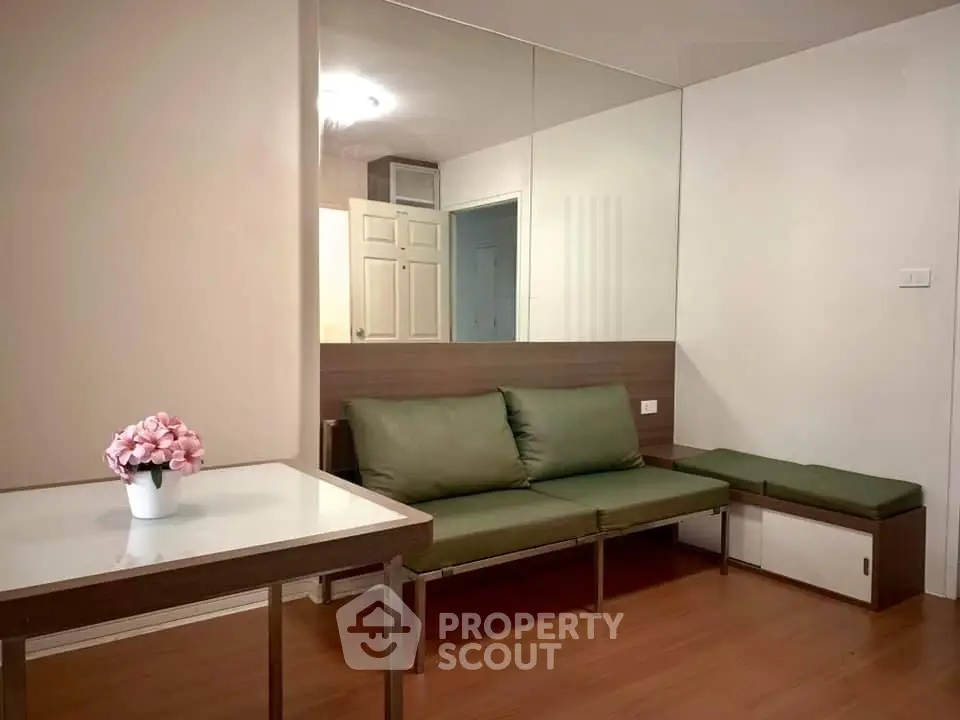 Modern living room with green sofa, wooden flooring, and decorative mirror wall.