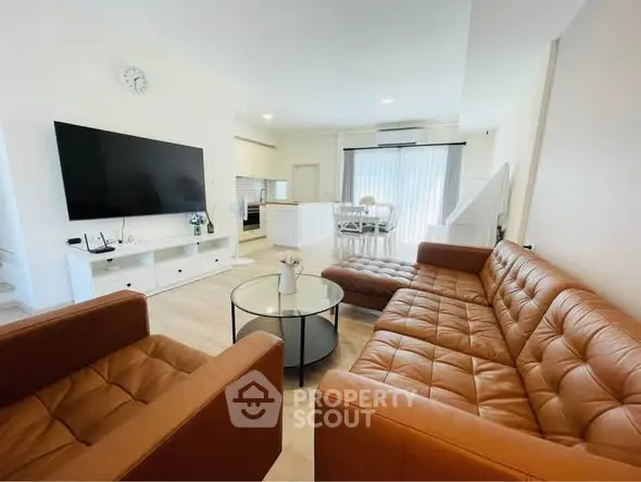 Spacious modern living room with leather sofa and large TV, open to dining area.