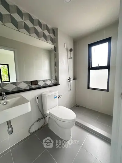 Modern bathroom with sleek design, featuring a large mirror and natural light from window.