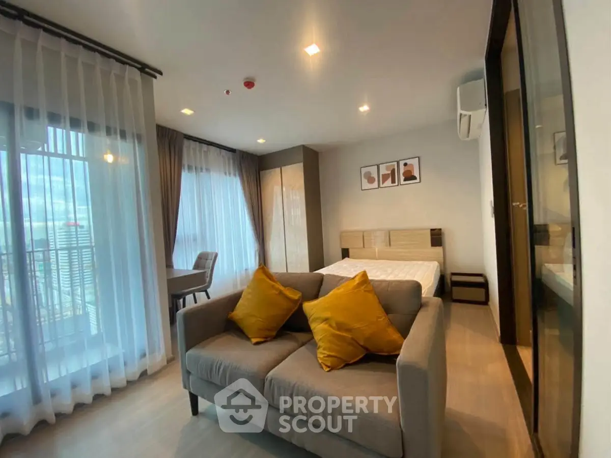 Modern studio apartment with cozy living area and large windows for natural light.