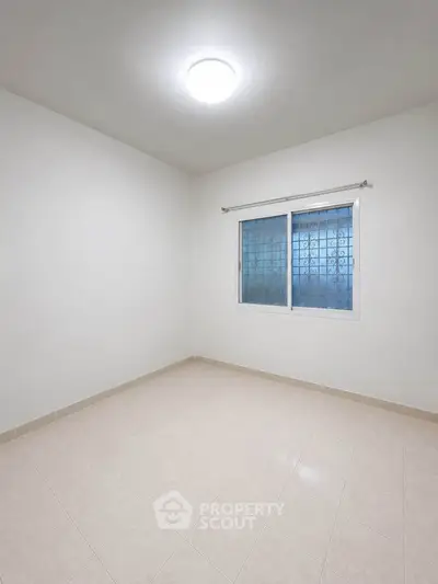 Spacious empty room with tiled floor and large window, perfect for customization.