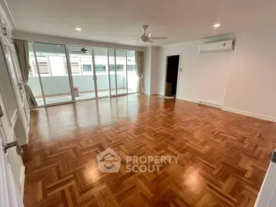Spacious living room with wooden flooring and large windows leading to a balcony, perfect for natural light.