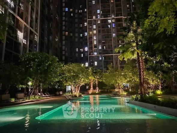 Luxurious apartment complex with illuminated pool and lush greenery at night.