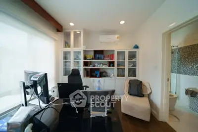 Modern home office with sleek desk, computer setup, and built-in bookshelves, adjacent to a stylish bathroom.