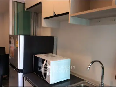 Modern kitchen with sleek cabinets, microwave, and stainless steel sink in a compact layout.