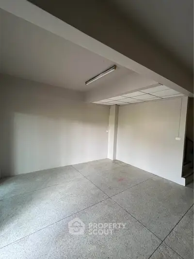 Spacious empty room with concrete flooring and fluorescent lighting, ideal for customization.