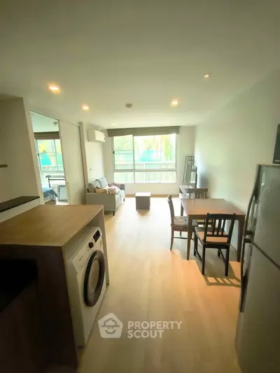 Modern living room with open kitchen and natural light, featuring a washing machine and dining area.
