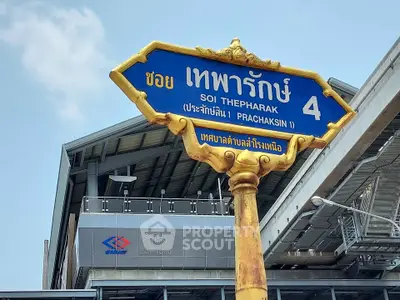 Street sign for Soi Thepharak 4 with modern building in background, ideal for urban real estate exploration.