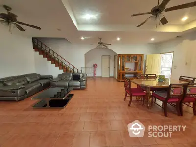 Spacious living room with terracotta tiled flooring, large leather sofas, wooden dining set, and an elegant staircase leading to the upper level.