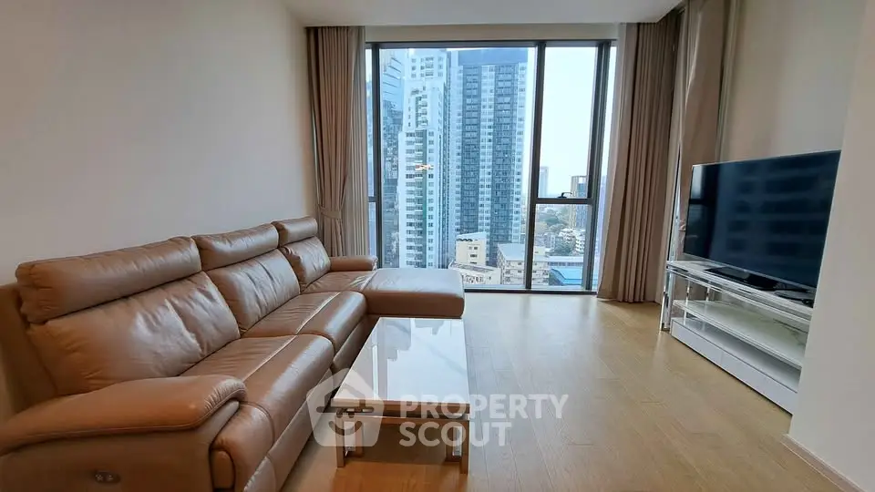 Spacious living room with modern leather sofa and stunning city view through large windows.