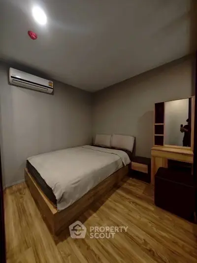 Cozy bedroom with modern furnishings and wooden flooring, featuring a comfortable bed and air conditioning.