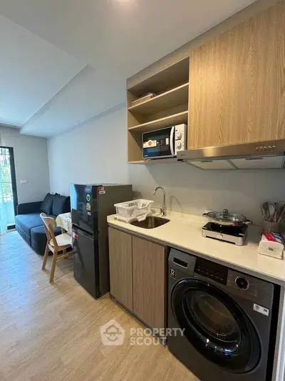 Modern kitchen with washing machine and cozy living area in open layout apartment.