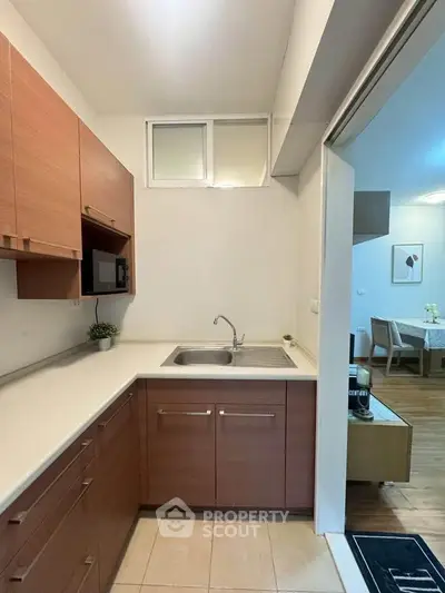 Modern kitchen with wooden cabinets and open layout leading to dining area.