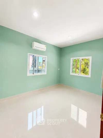 Bright empty room with mint green walls and large windows, featuring a modern air conditioning unit.