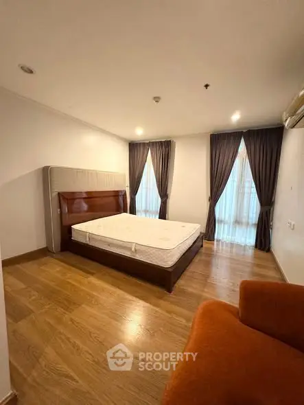 Spacious bedroom with wooden flooring and elegant curtains in a modern apartment.