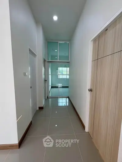 Spacious hallway with modern design and glossy tiled flooring leading to a bright room.