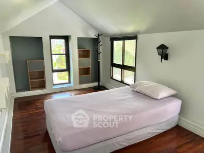 Charming attic bedroom with wooden floors and large windows offering natural light.