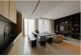 Modern living room with sleek design and open kitchen layout, featuring a large TV and stylish shelving.