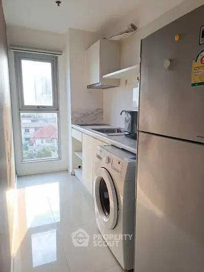 Bright kitchen with washing machine and fridge, featuring a large window with city view.