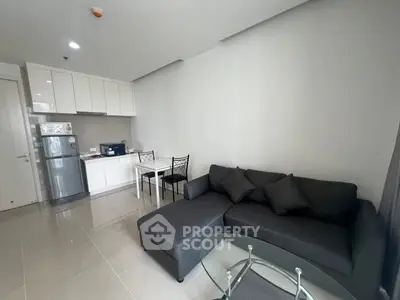 Modern living room with sleek kitchen, cozy sofa, and glass coffee table in open layout apartment.