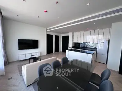 Modern open-layout living room with sleek kitchen and dining area, featuring contemporary furniture and large TV.