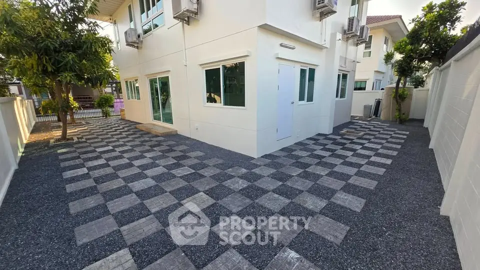 Modern two-story house with spacious checkered patio and lush greenery