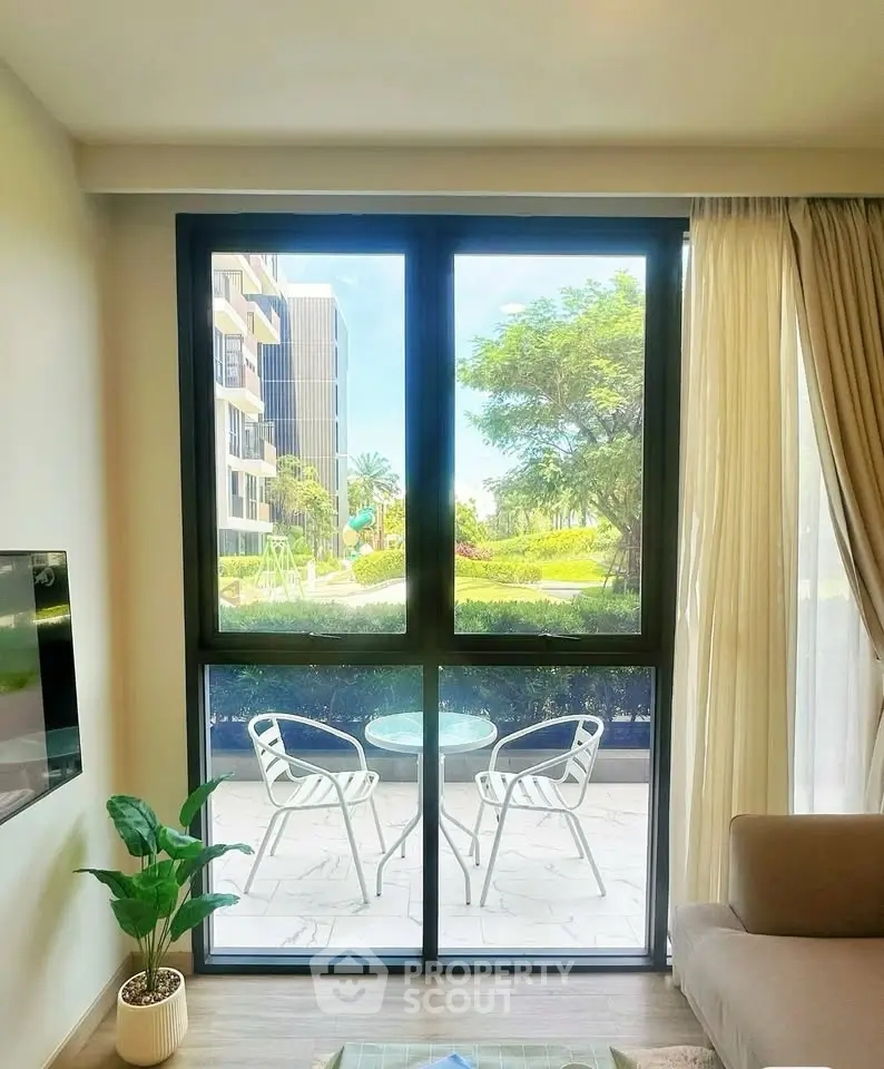 Bright living room with large window overlooking garden and patio, modern furniture, and natural light.