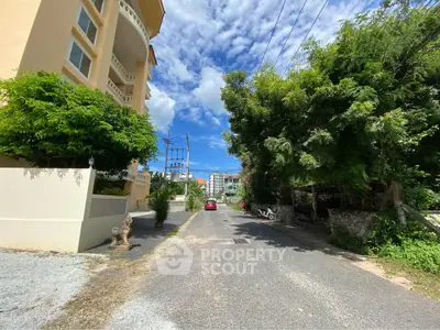 Charming residential street view with lush greenery and modern apartment building under a bright blue sky.