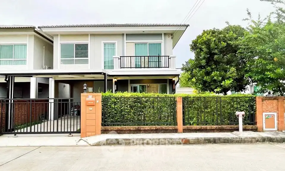Modern two-story house with balcony and lush greenery in a serene neighborhood.