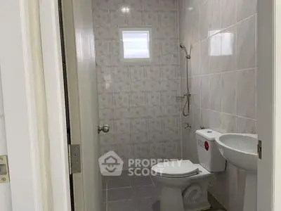 Compact bathroom with modern fixtures and tiled walls, featuring a toilet, sink, and shower area.