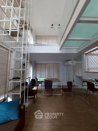Modern living room with high ceiling and mezzanine, featuring stylish furniture and large windows.