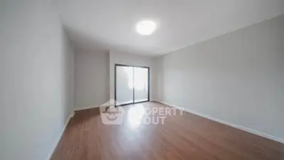 Spacious empty room with wooden flooring and large window, perfect for customization.
