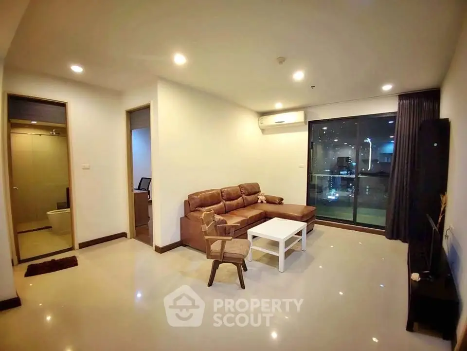 Spacious modern living room with leather sofa and large window offering city view.